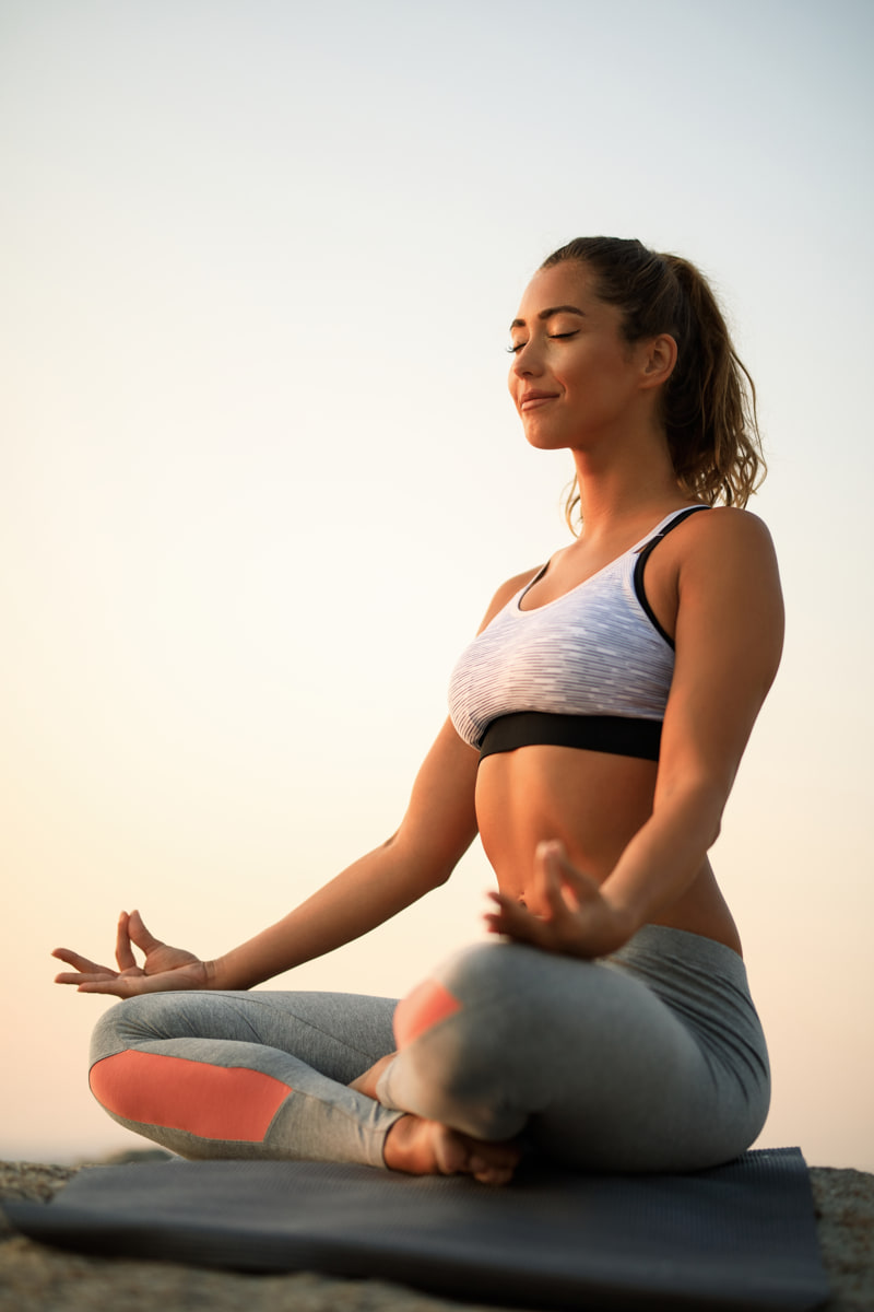 vista-angulo-mujer-meditando-ojos-cerrados-mientras-ejercita-yoga-roca-contra-cielo-copie-espacio